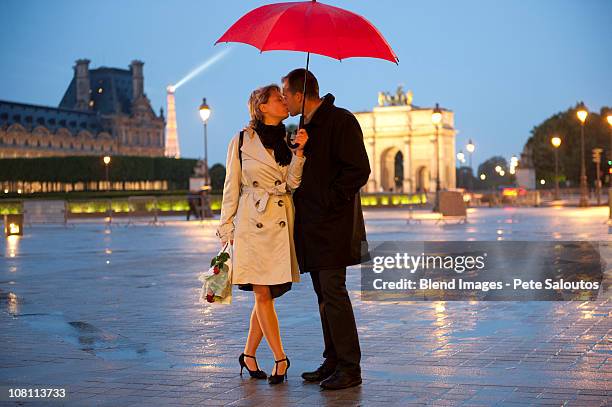 caucasian couple kissing in rain at night near the louvre - couple paris stock pictures, royalty-free photos & images