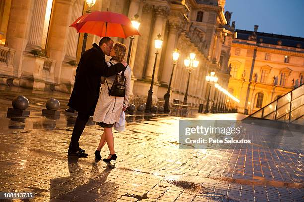 caucasian couple kissing in rain at night at the louvre - couples kissing shower photos et images de collection