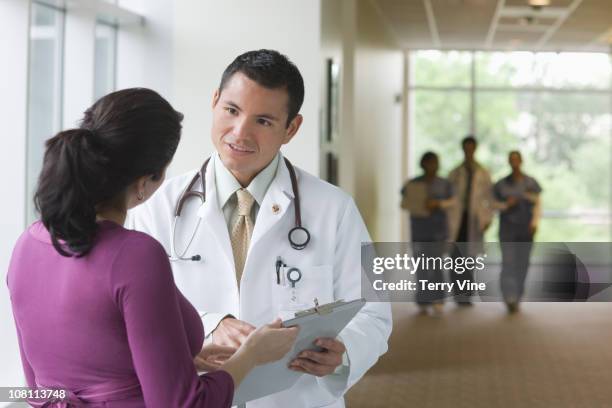 hispanic doctor talking to co-worker in hospital corridor - man looking at foreground stock pictures, royalty-free photos & images