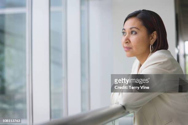 hispanic businesswoman leaning against railing - casual woman pensive side view stockfoto's en -beelden