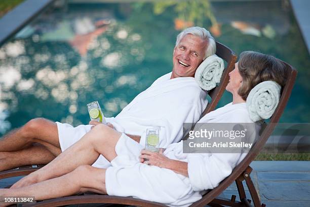 couple in robes relaxing in lounge chairs at poolside - resort swimming pool stockfoto's en -beelden