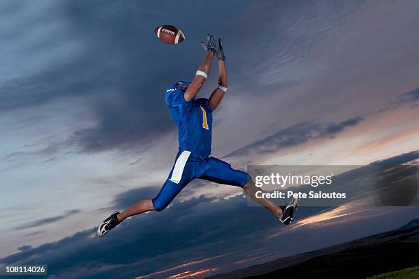 mixed race football player jumping in mid-air catching football - american football player catch stock pictures, royalty-free photos & images