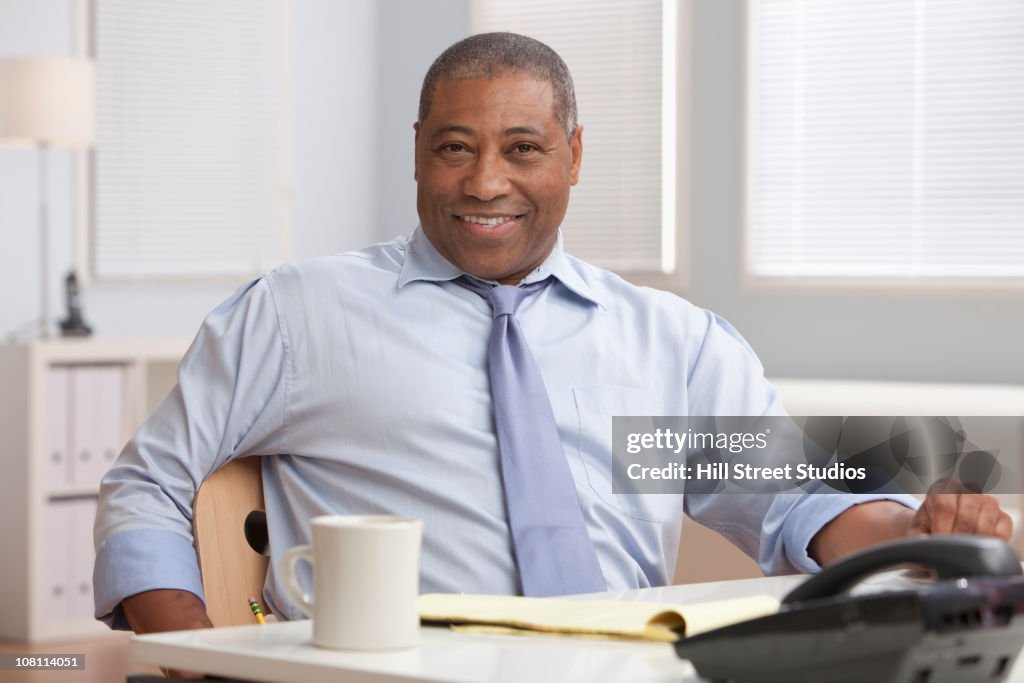 Sorridente preto Empresário sentado na mesa de Escritório