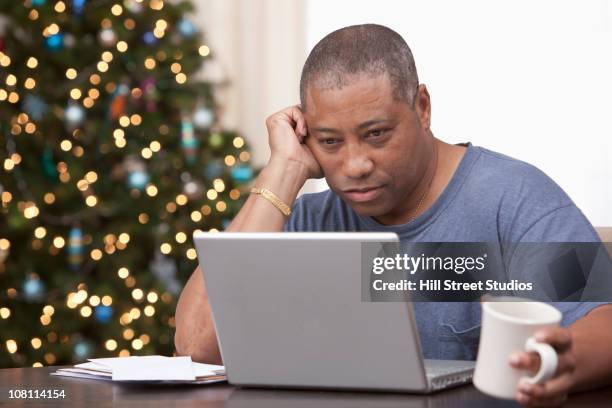 black man using laptop with christmas tree in background - african people buying a christmas tree stockfoto's en -beelden