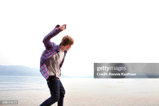 hombre caucásico rebotar piedras en el agua en el lago - throwing fotografías e imágenes de stock