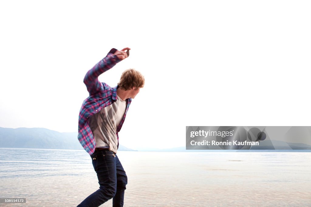 Caucasian man skimming stones on lake