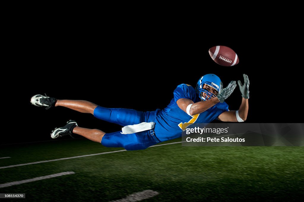 Mixed race football player jumping in mid-air catching football