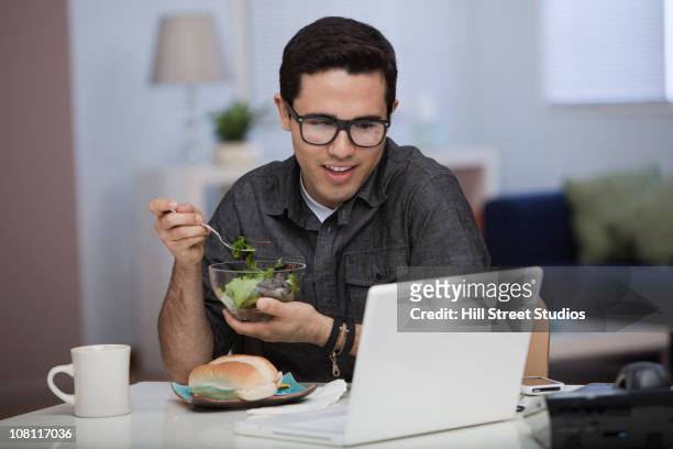 hispanic man eating lunch and working on laptop - telecommuting eating stock pictures, royalty-free photos & images