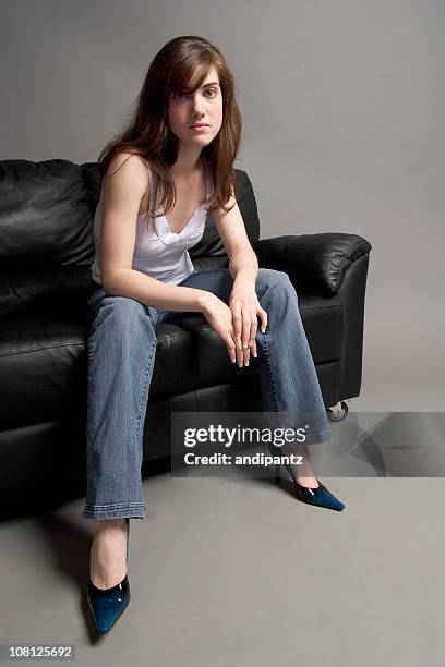 serious young woman sitting on black leather couch - studio shot lonely woman stock pictures, royalty-free photos & images