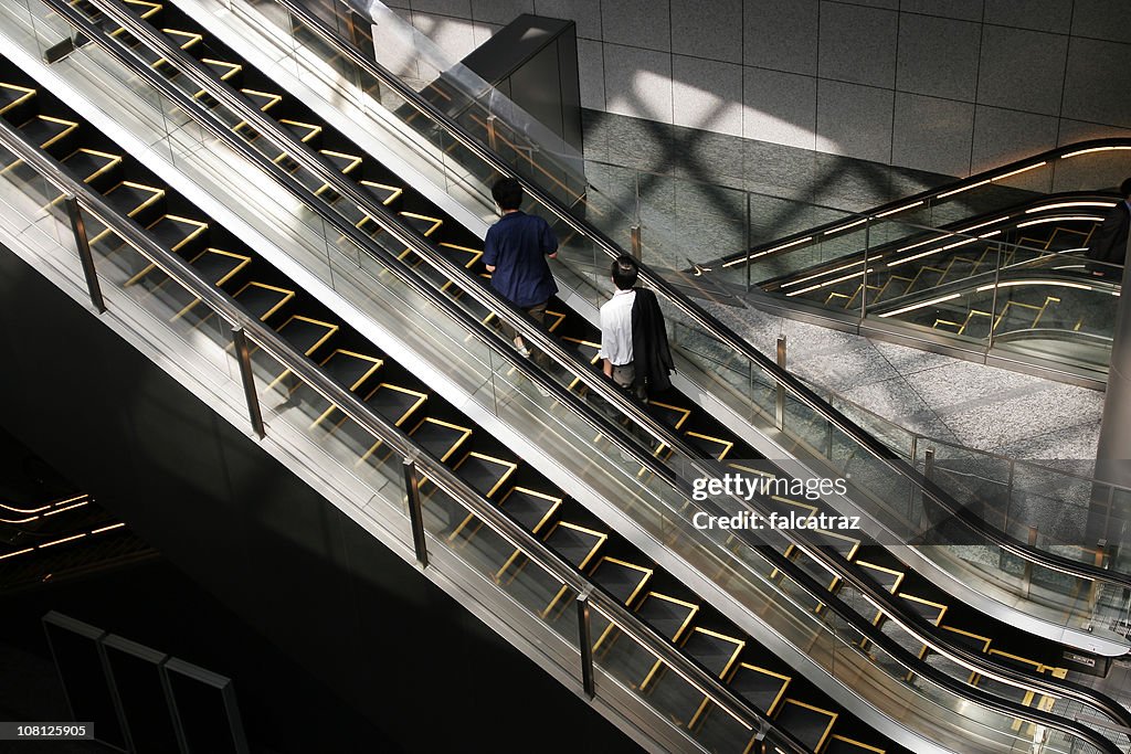 Two People Riding Escalator in Building