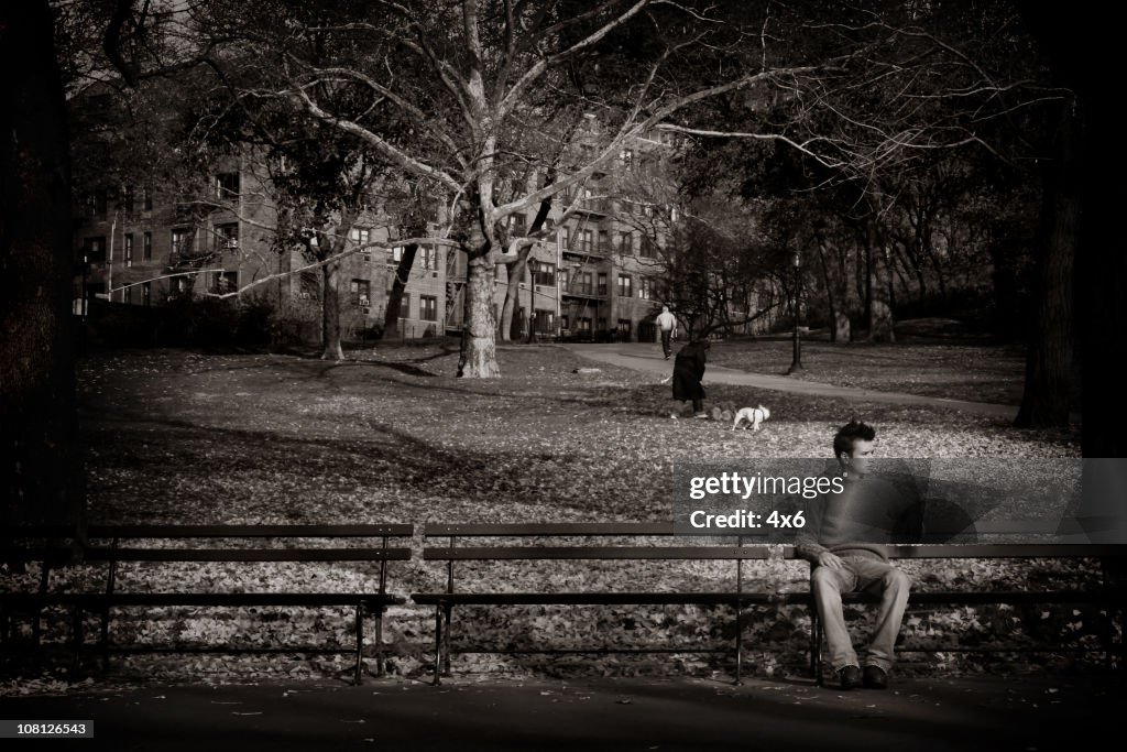 Blanco y negro de hombre joven sentado en el banco del parque