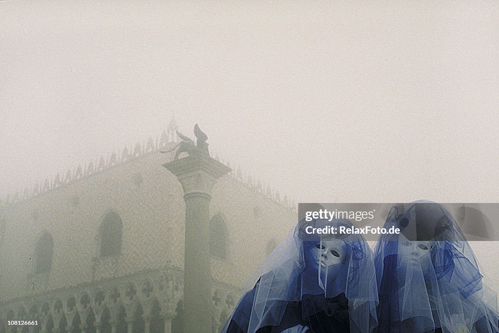 Two mysterious carnival masks with blue veil in foggy Venice