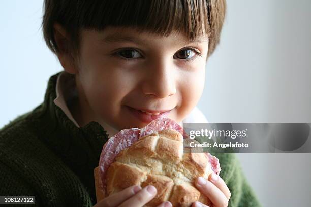 lächelnden kleinen jungen kleinkind ernährung salami-sandwich auf brötchen - wurst stock-fotos und bilder