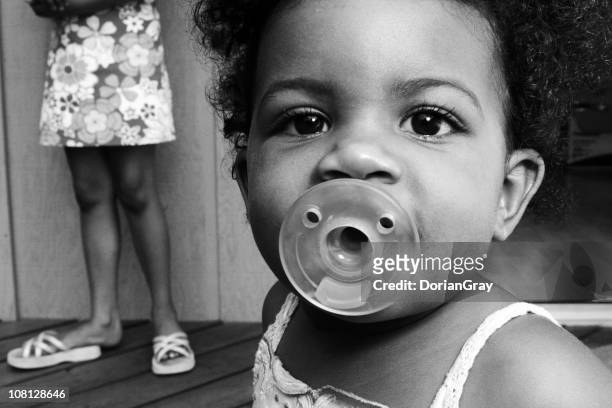 portrait of baby girl with sister's feet in background - baby accessories the dummy stock pictures, royalty-free photos & images