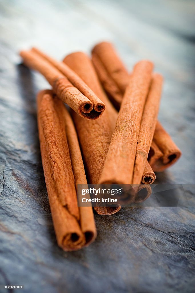 Pile of cinnamon sticks on a dark textured surface