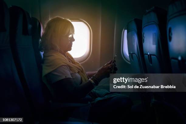 senior woman using a smartphone on a plane - comfortable flight stock pictures, royalty-free photos & images