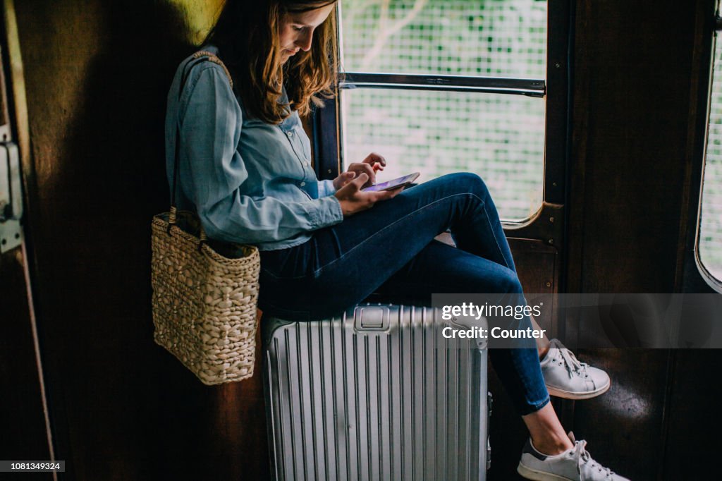 Woman sitting on suitcase in train looking at smart phone