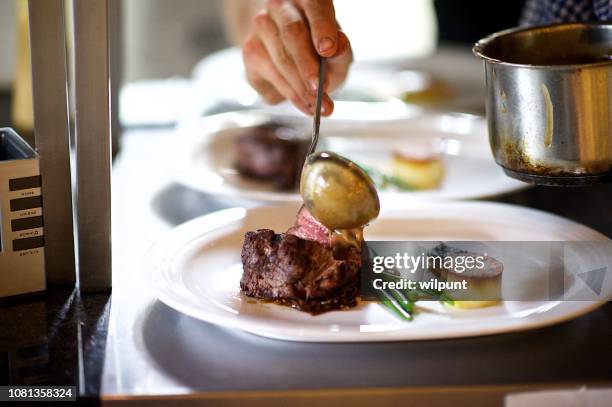 steak on a plate being prepared in a chef's kitchen sauce being poured - steakhouse stock pictures, royalty-free photos & images