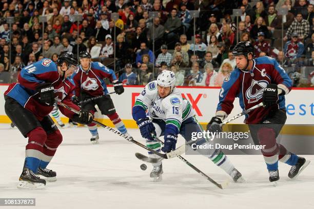 Tanner Glass of the Vancouver Canucks tries to control the puck between Tomas Fleischmann and Adam Foote of the Colorado Avalanche at the Pepsi...