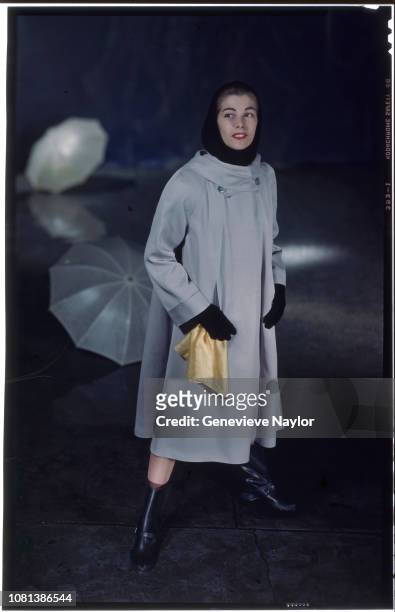 Woman models a cape-style raincoat with several umbrellas around her.