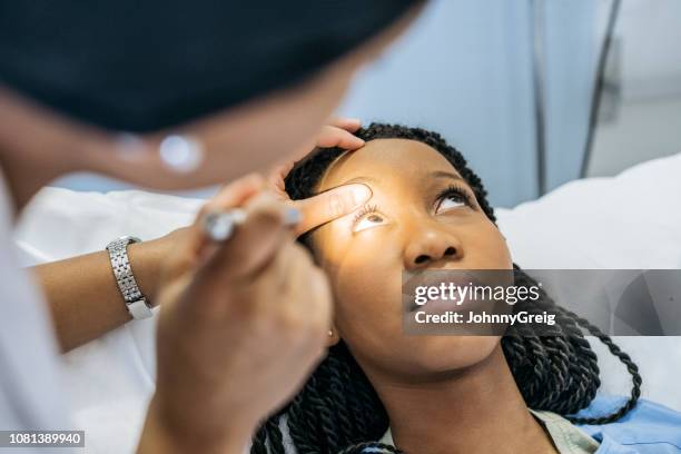 young woman in hospital having eye examination looking up - doctor shining light in eyes stock pictures, royalty-free photos & images