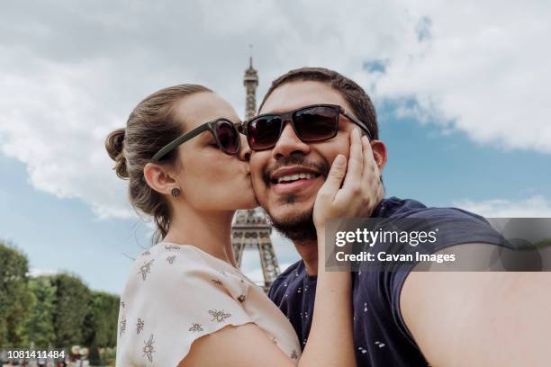 portrait of girlfriend kissing boyfriend against eiffel tower in city - couple paris stockfoto's en -beelden