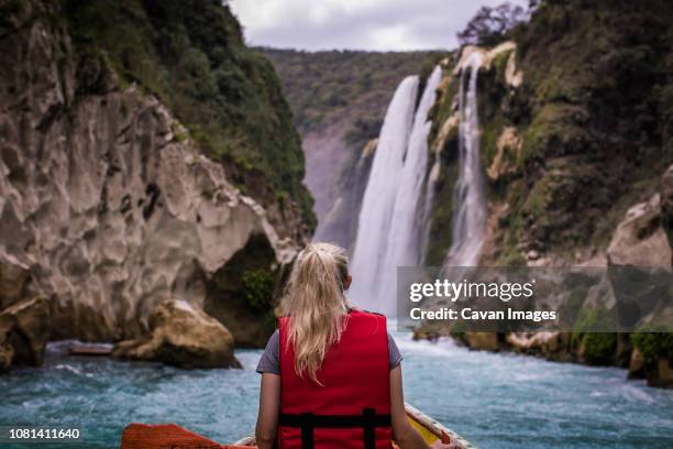 rear view of woman sitting in boat on river against waterfall - life jacket isolated stock pictures, royalty-free photos & images