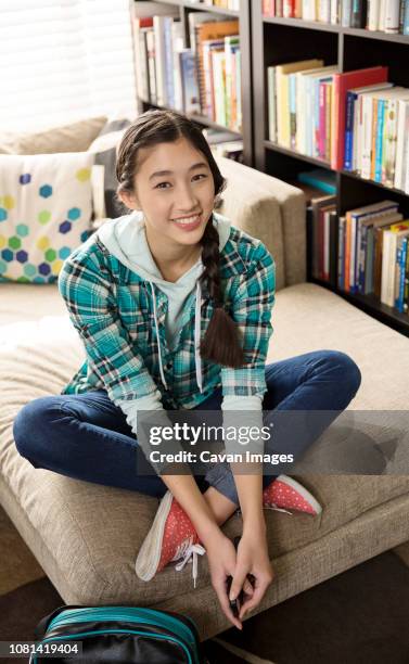 full length of cheerful teenage girl sitting on couch at home - teen packing suitcase stock pictures, royalty-free photos & images