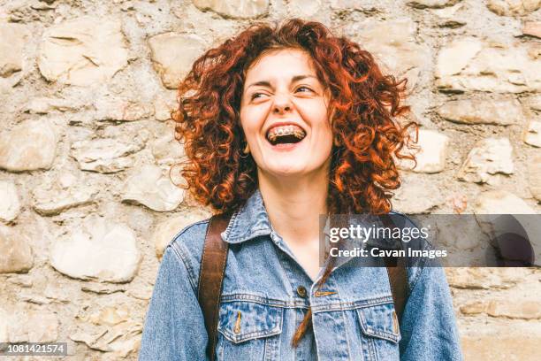 close-up of happy woman looking away while standing by wall - zahnspange frau stock-fotos und bilder