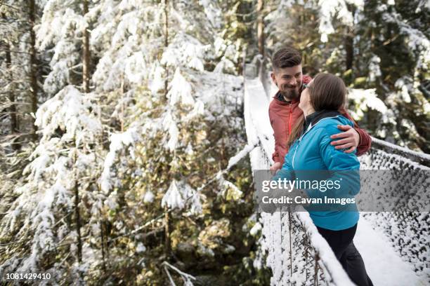 couple standing on footbridge amidst forest at lynn canyon park during winter - british columbia winter stock pictures, royalty-free photos & images