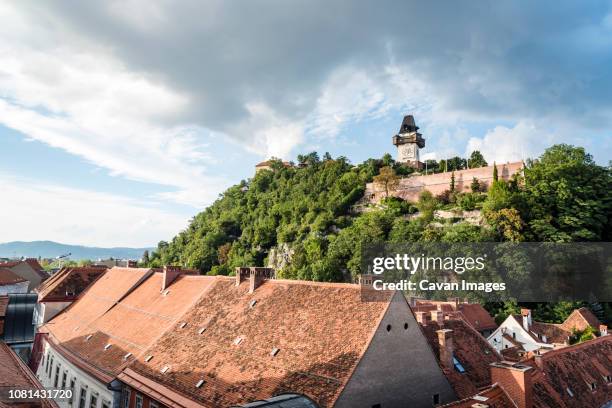 houses in town against schlossberg and cloudy sky - turmuhr stock-fotos und bilder