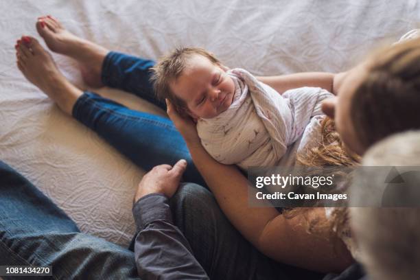 overhead view of parents with newborn daughter sitting on bed at home - father holding sleeping baby stockfoto's en -beelden