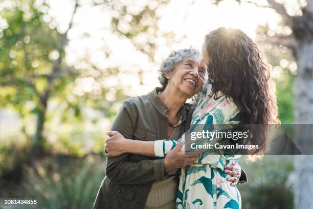 happy mother and daughter embracing while standing at park - aging happy stockfoto's en -beelden