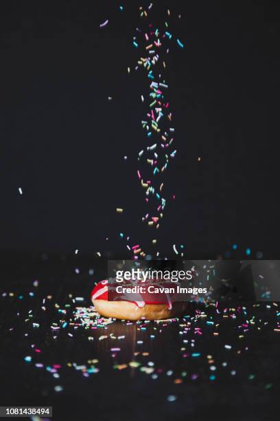 sprinkles sprinkling on donut at wooden table against black background - gekleurde hagelslag stockfoto's en -beelden