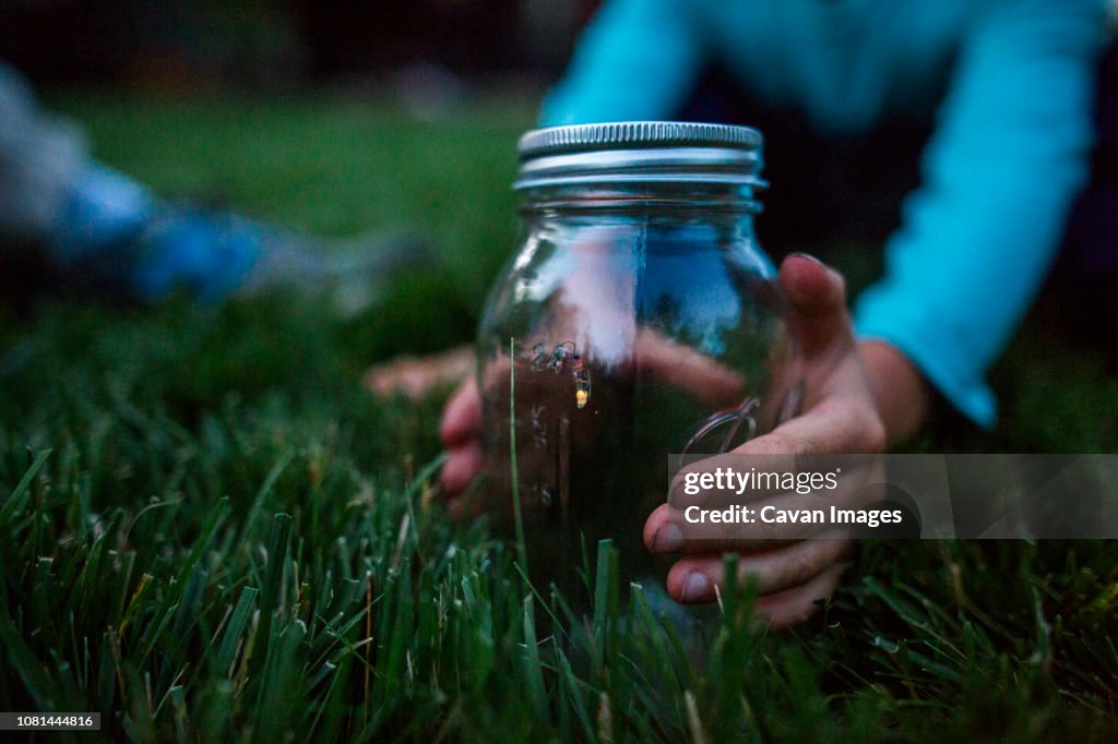 Cropped hands of boy holding glass jar with firefly on grassy field