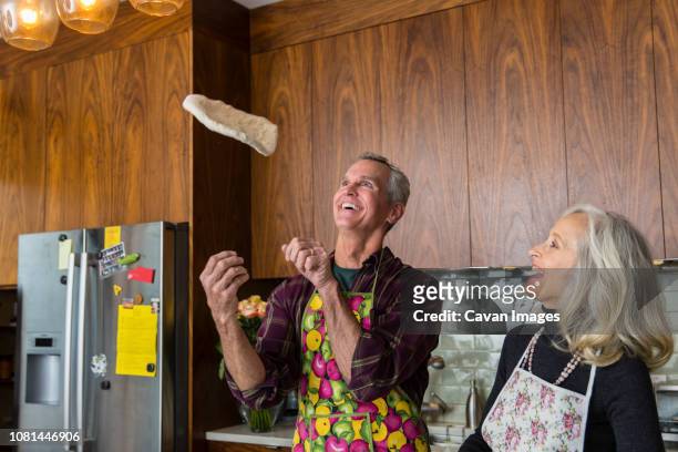 cheerful man tossing pizza dough while preparing food by woman in kitchen at home - pizza toss foto e immagini stock