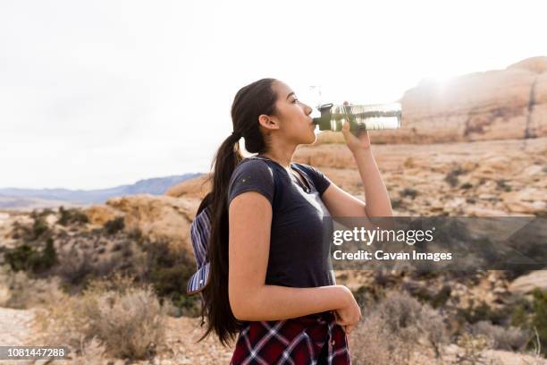 woman with backpack drinking water while standing by rock formation against clear sky - nevada hiking stock pictures, royalty-free photos & images