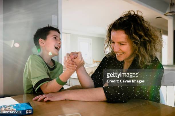 playful mother arm wrestling with son on table at home - echar un pulso fotografías e imágenes de stock