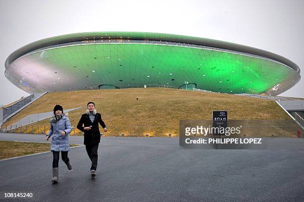 Man and a woman run by the illuminated 18,500-seat Mercedes-Benz Arena in Shanghai on January 19, 2011. Entertainment giant AEG, the operator of Los...