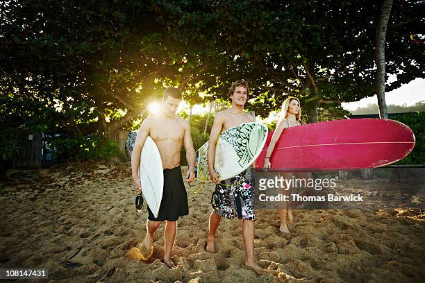 Three siblings walking onto beach with surfboards
