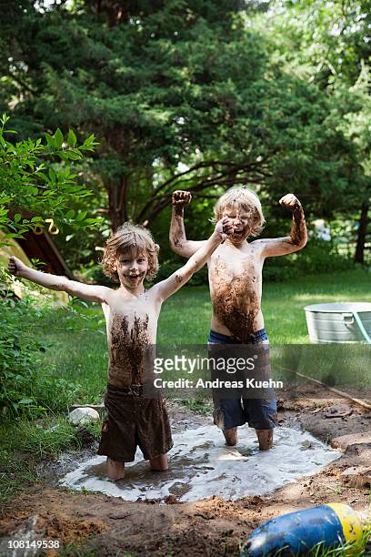 two little boys standing in a mud hole. - garden of laughs stockfoto's en -beelden