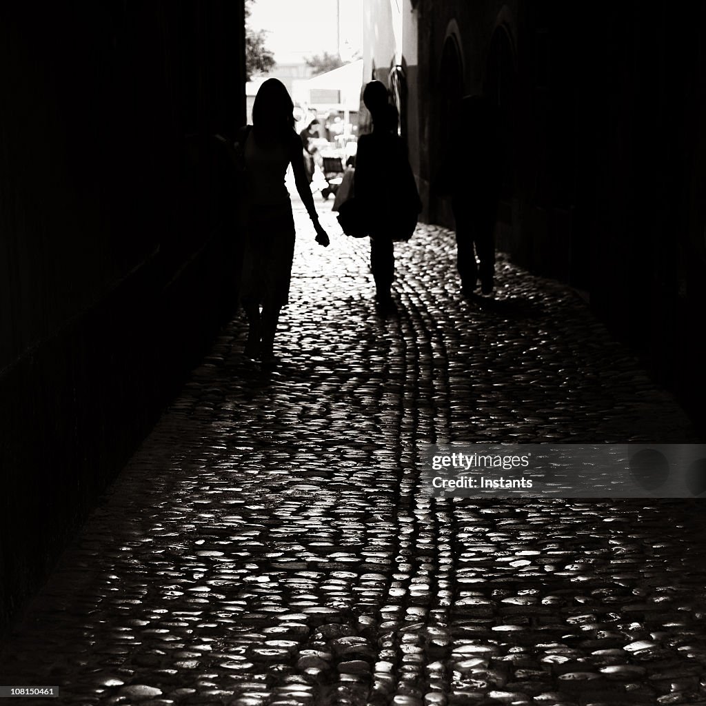 Silhouette of people walking down dark cobblestone alley