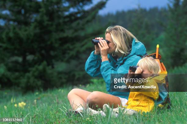mother and daughter look through binoculars while sitting in meadow - blue jacket stock pictures, royalty-free photos & images