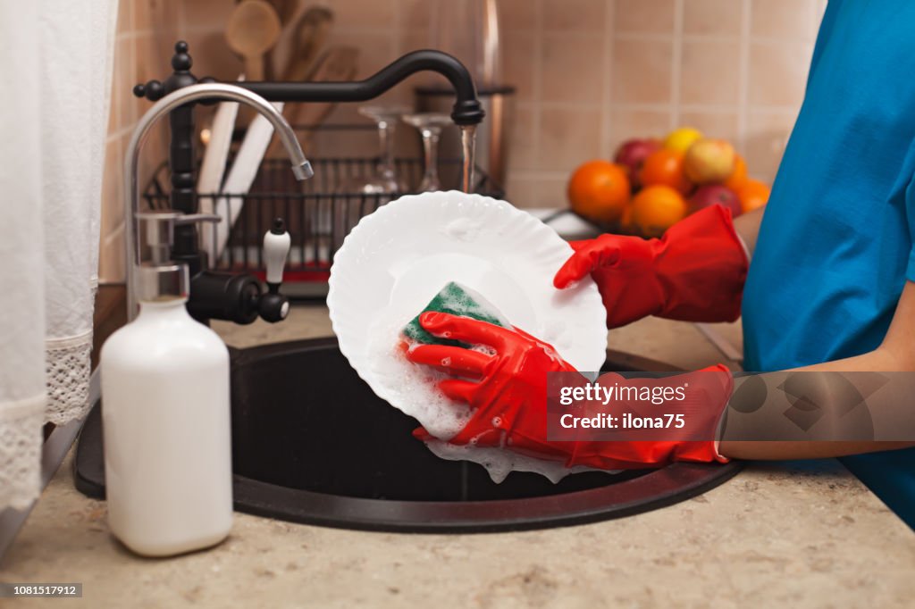 Washing the dishes after a meal - child hands scrubbing a plate with a sponge, shallow depth