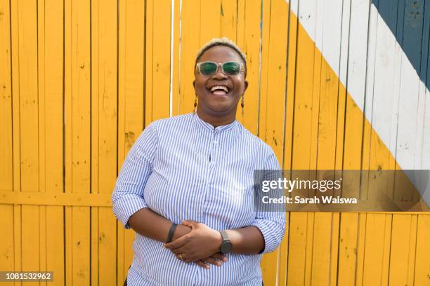 portrait of black woman in front of a yellow wall laughing - kenya woman stock pictures, royalty-free photos & images