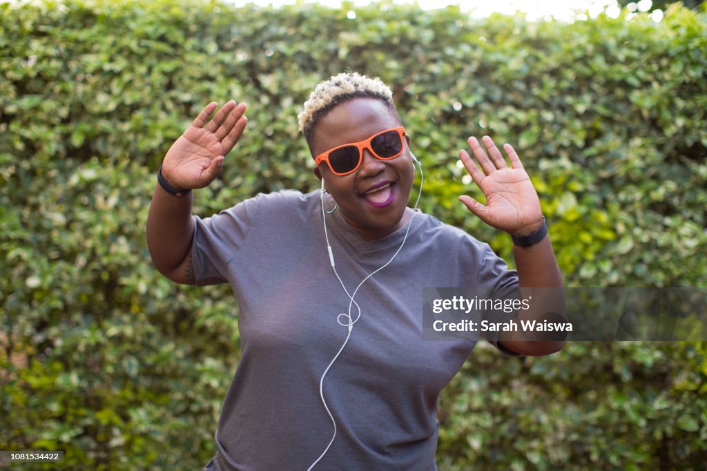 Portrait of a black woman listening to music outside with hands in the air