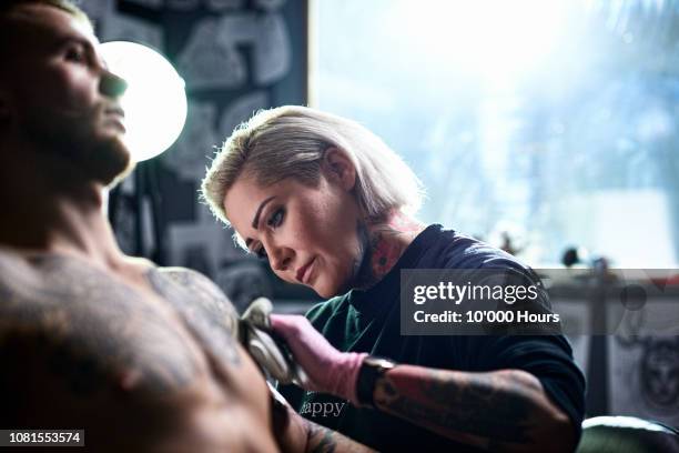 female tattooist applying tattoo to male customer - tatoo foto e immagini stock