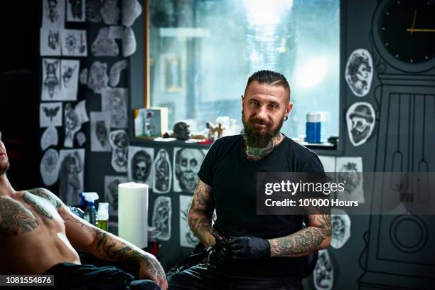 portrait of male tattoo artist in tattoo parlour facing camera - tattoo artist portrait stock-fotos und bilder