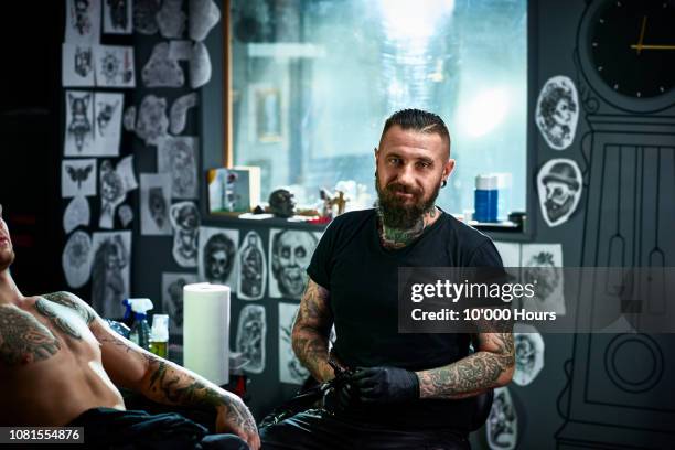 portrait of male tattoo artist in tattoo parlour facing camera - tätowierung stock-fotos und bilder