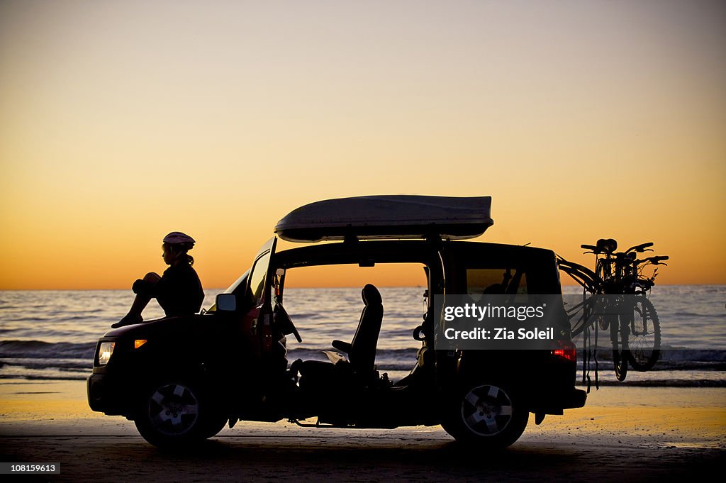 Girl with car and bikes, sunset beach silhouette